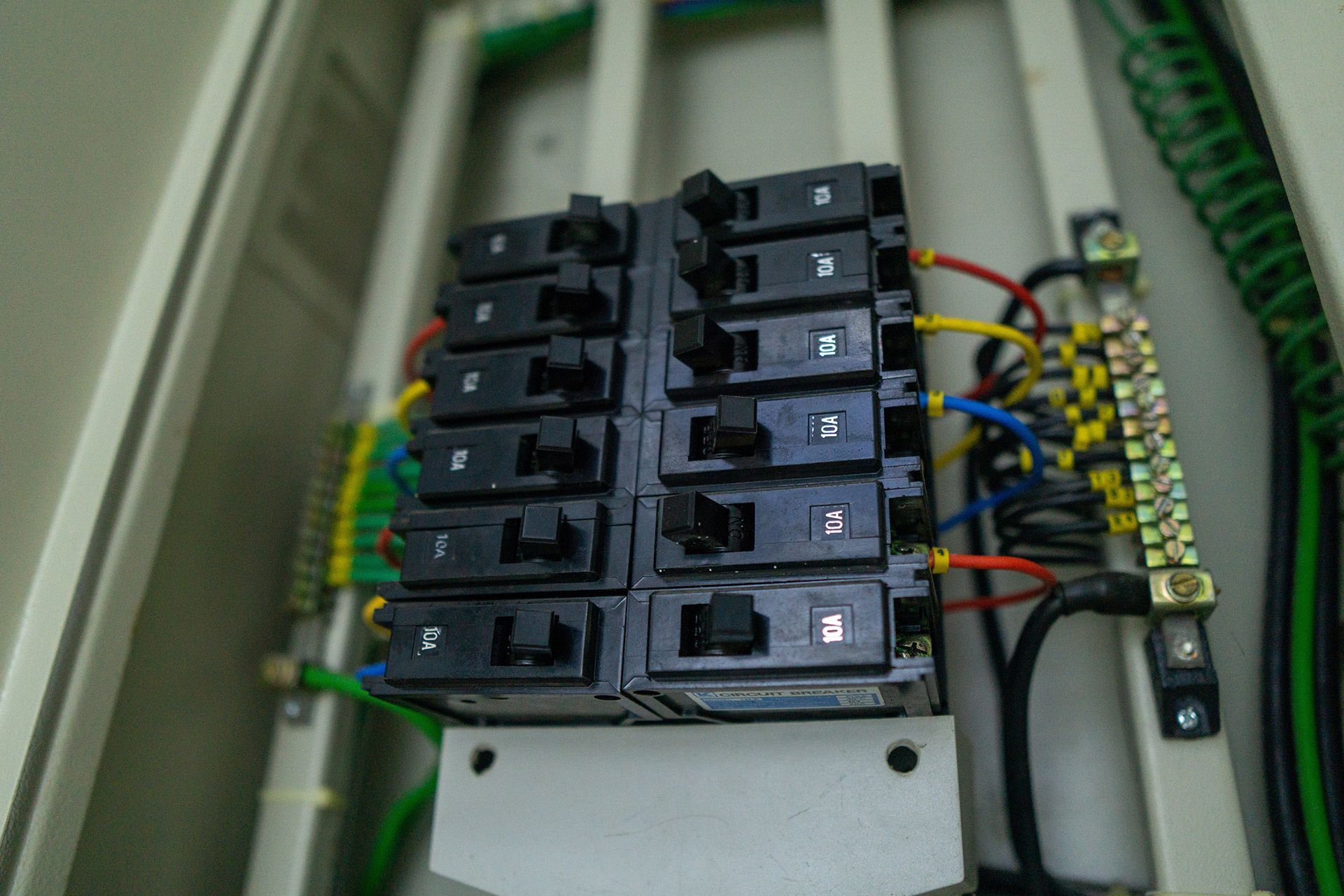 Electrical breaker panel with rows of black switches and colored wires inside a cabinet