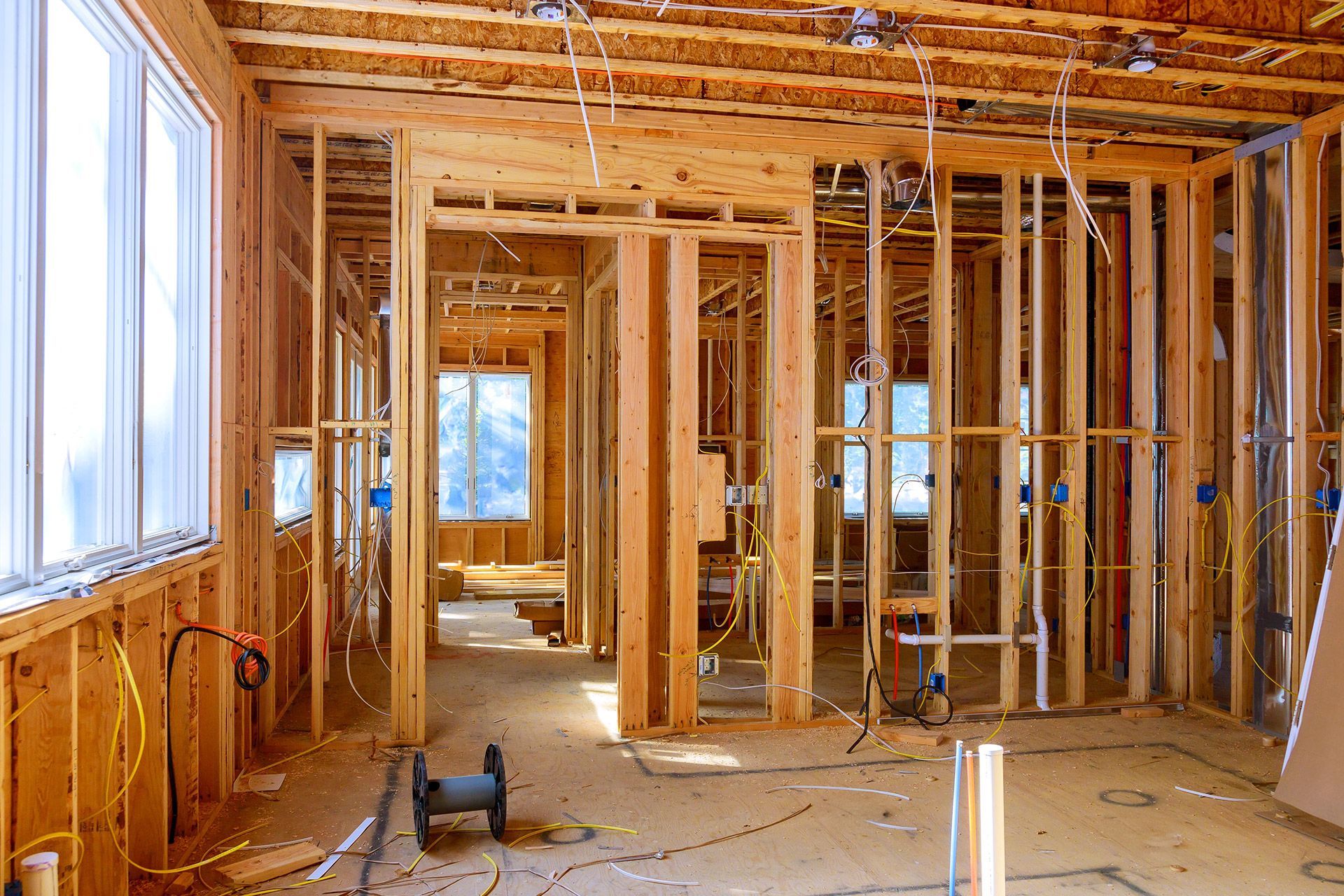 Interior of a house under construction with exposed wooden framing, wiring, and unfinished floors.