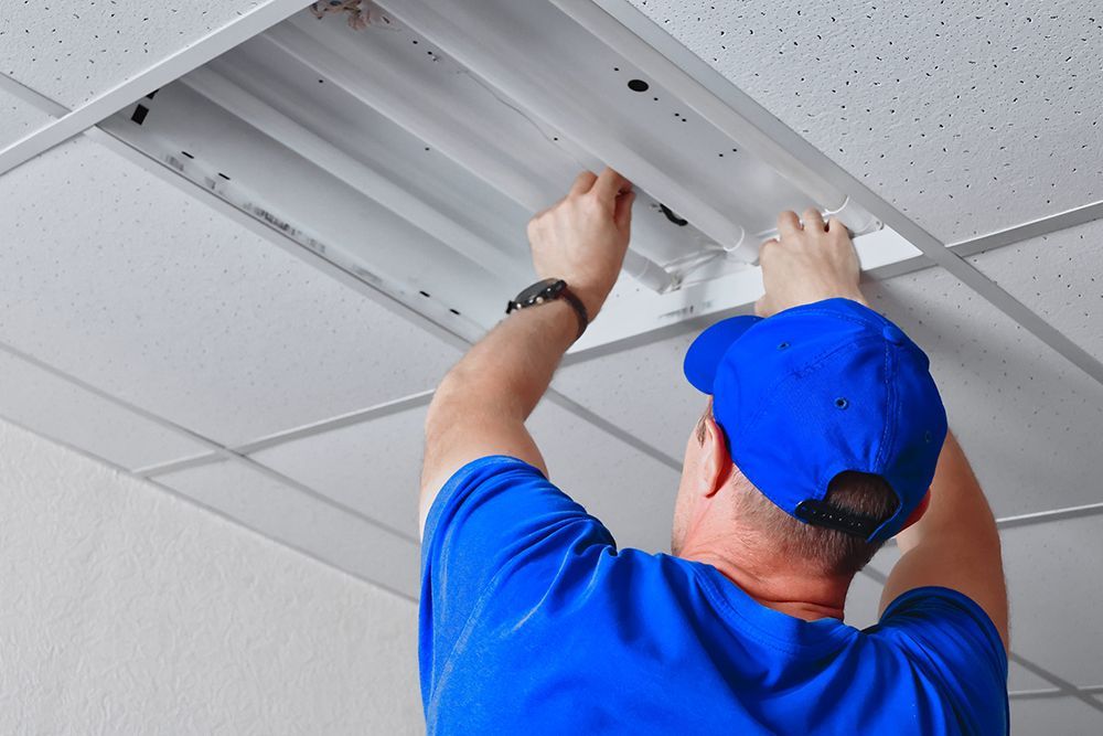 Technician in blue shirt installing a ceiling light fixture on a drop ceiling