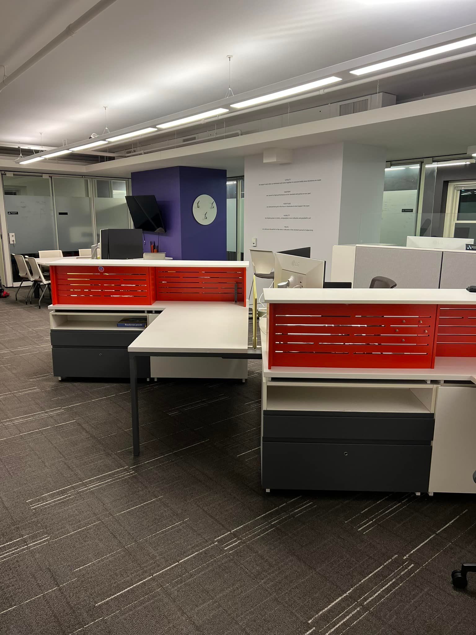 Modern office with red-and-white desks, black carpet, and purple wall accents in a quiet workspace