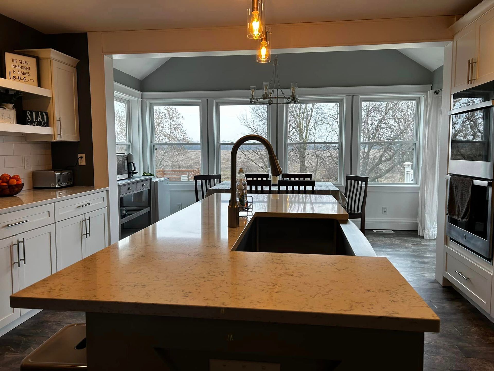 Modern kitchen with large island, black faucet, white cabinets, and dining area by bright windows