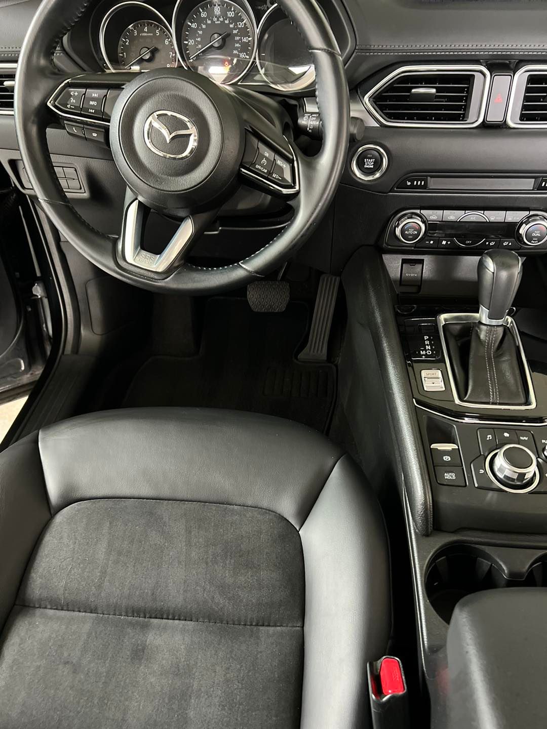 Mazda car interior with steering wheel, dashboard, center console, and black leather seat