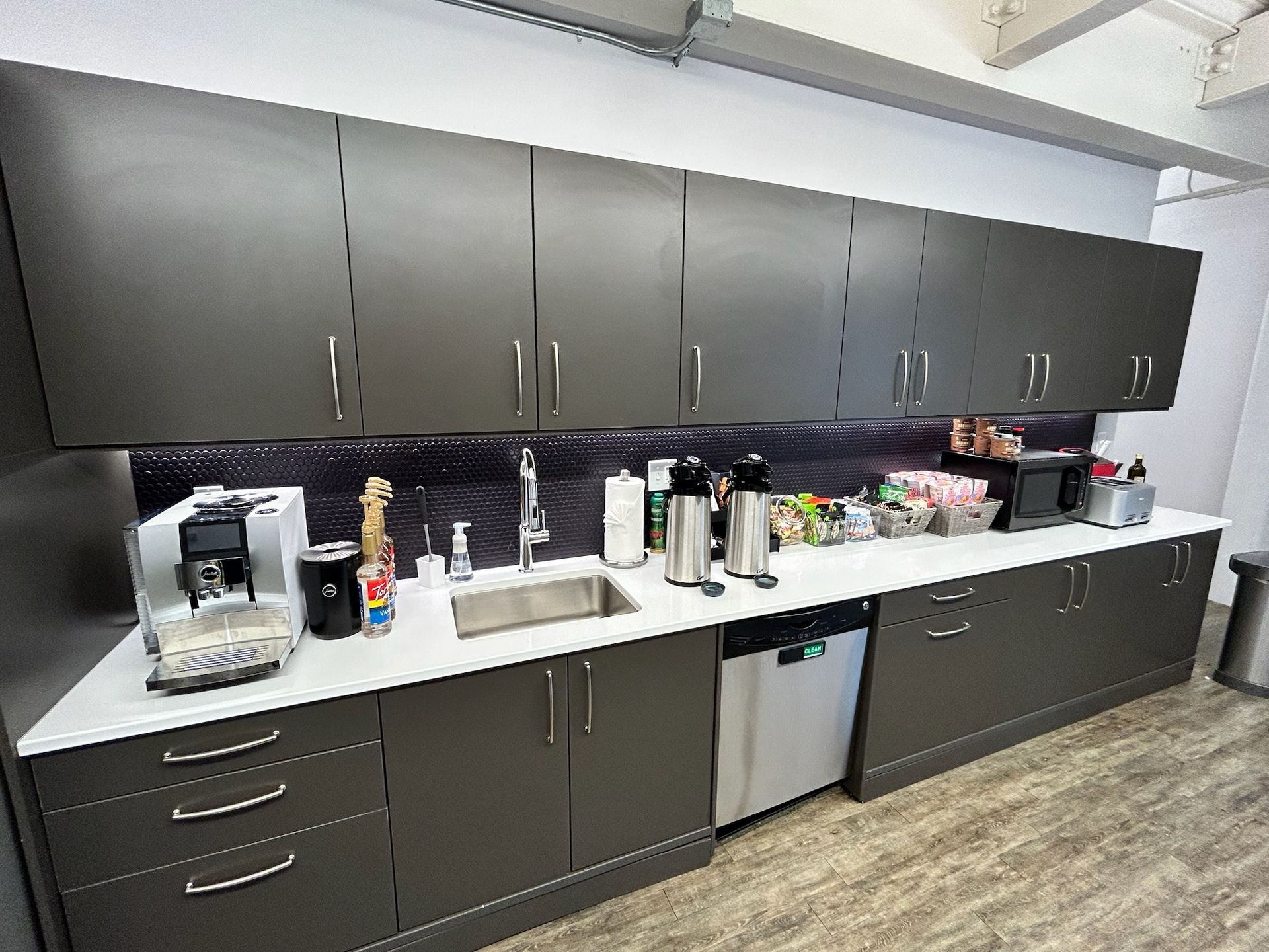 Office kitchenette with dark cabinets, white countertops, coffee makers, sink, and mini fridge