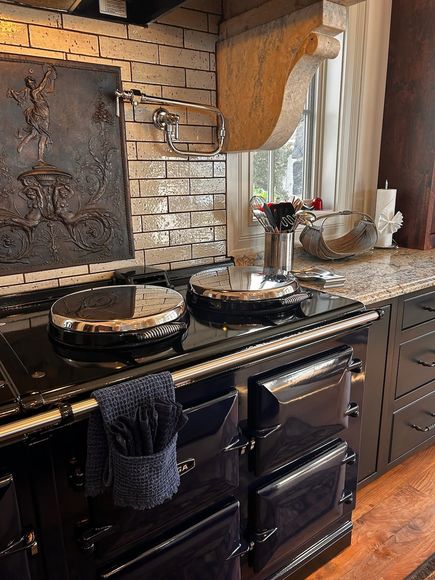 Kitchen with black stove, decorated trays, and granite countertop beneath a window with curtains