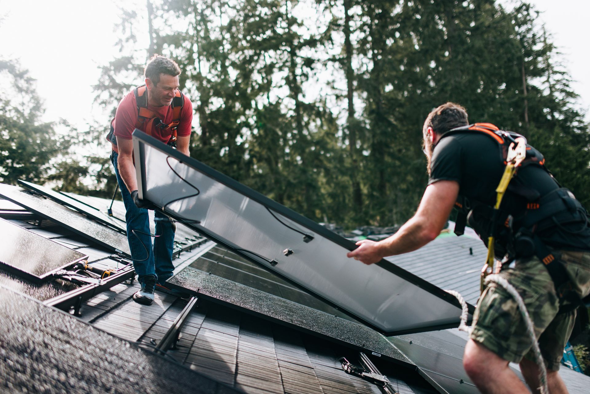 Two workers installing solar panel on a rooftop, with safety harnesses.