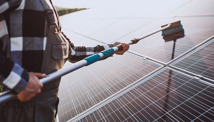 Technician cleaning solar panels with a brush