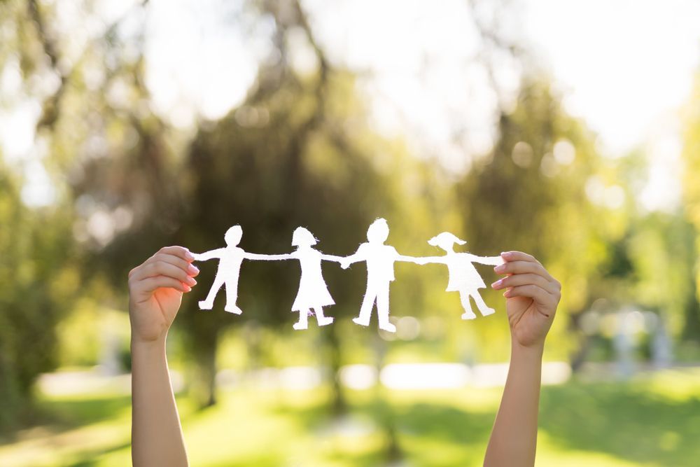 Hands holding a white paper family chain outdoors in a sunny park. — PoDDSS in Hyde Park, QLD