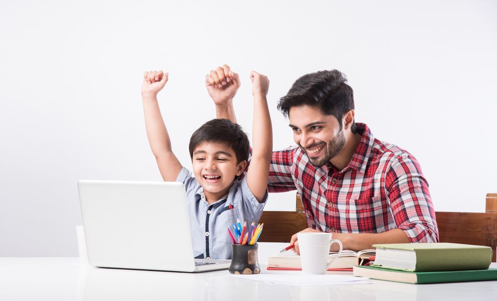 A Child Celebrates With Raised Arms While Sitting at a Laptop Next to an Adult — PoDDSS in Hyde Park, QLD