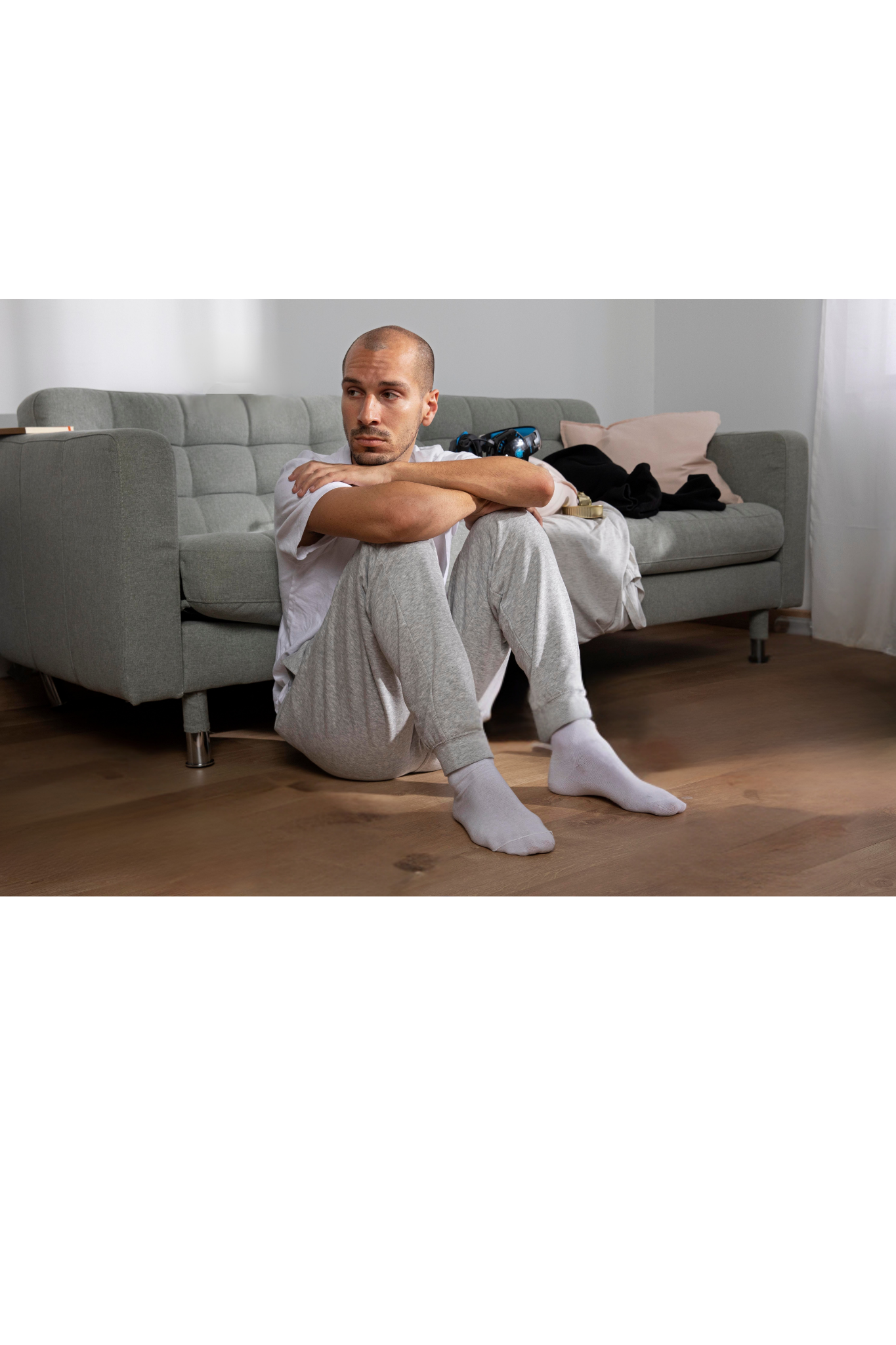 Person sitting on a wooden floor in front of a gray couch, hugging their knees and looking at the camera. — PoDDSS in Hyde Park, QLD