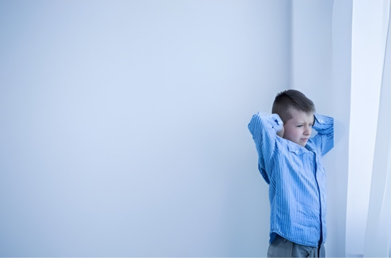 Young child in a blue shirt leaning against a white wall with hands behind head near a curtain — PoDDSS in Mount Isa, QLD