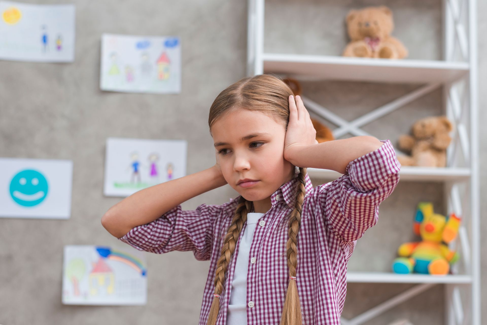 Child covering ears in a classroom, with drawings and toys on shelves in the background — PoDDSS in Charters Towers, QLD