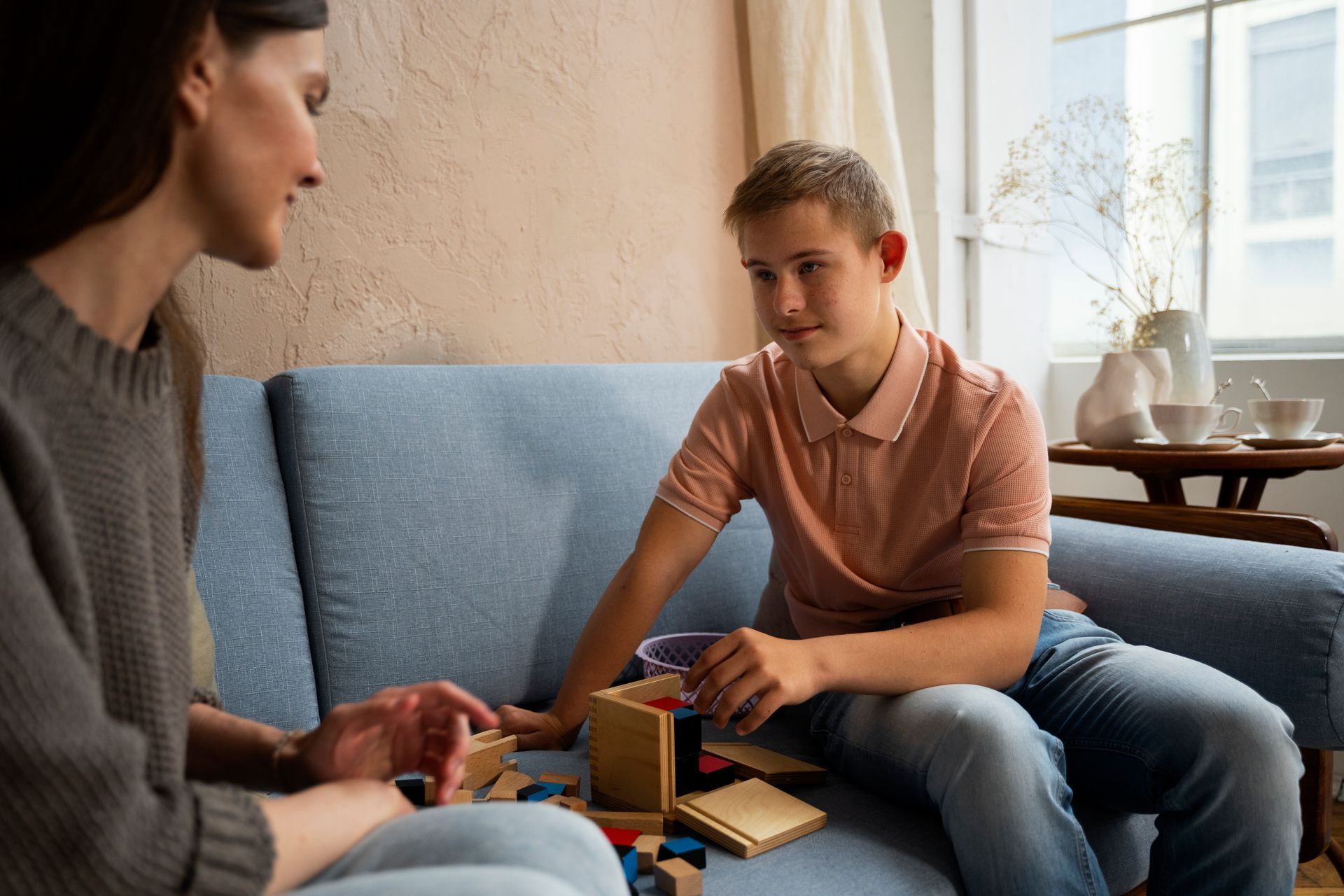 Two people sit on a couch, playing a board game by a bright window. — PoDDSS in Hyde Park, QLD