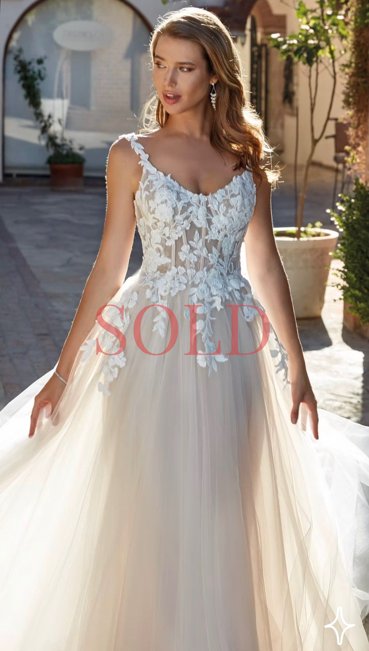 Woman in a white floral lace gown standing outdoors in sunlight.