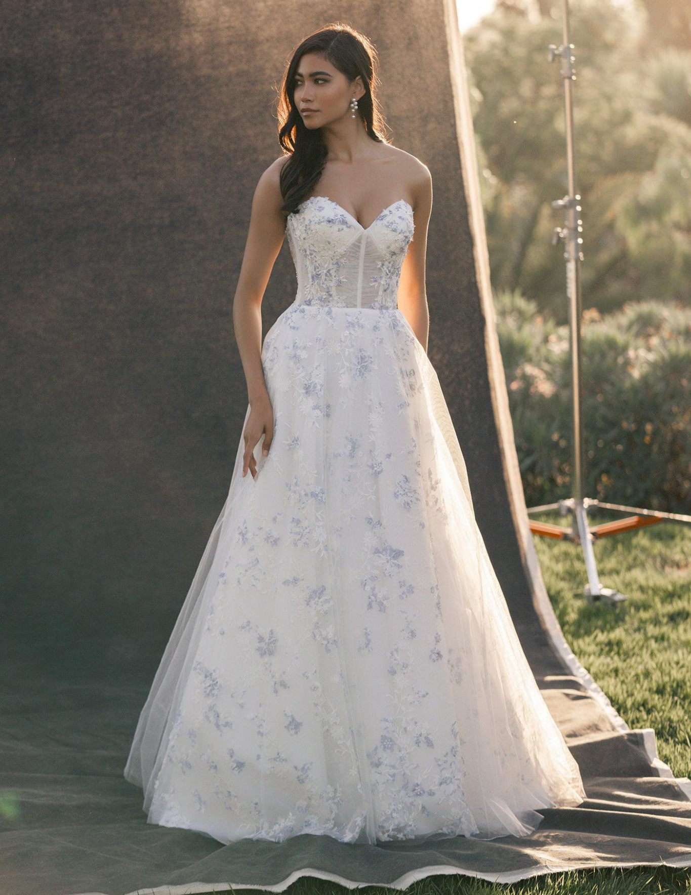 A strapless wedding dress with a lace bodice and a floor-length, fitted satin skirt, worn by a person posing outdoors.