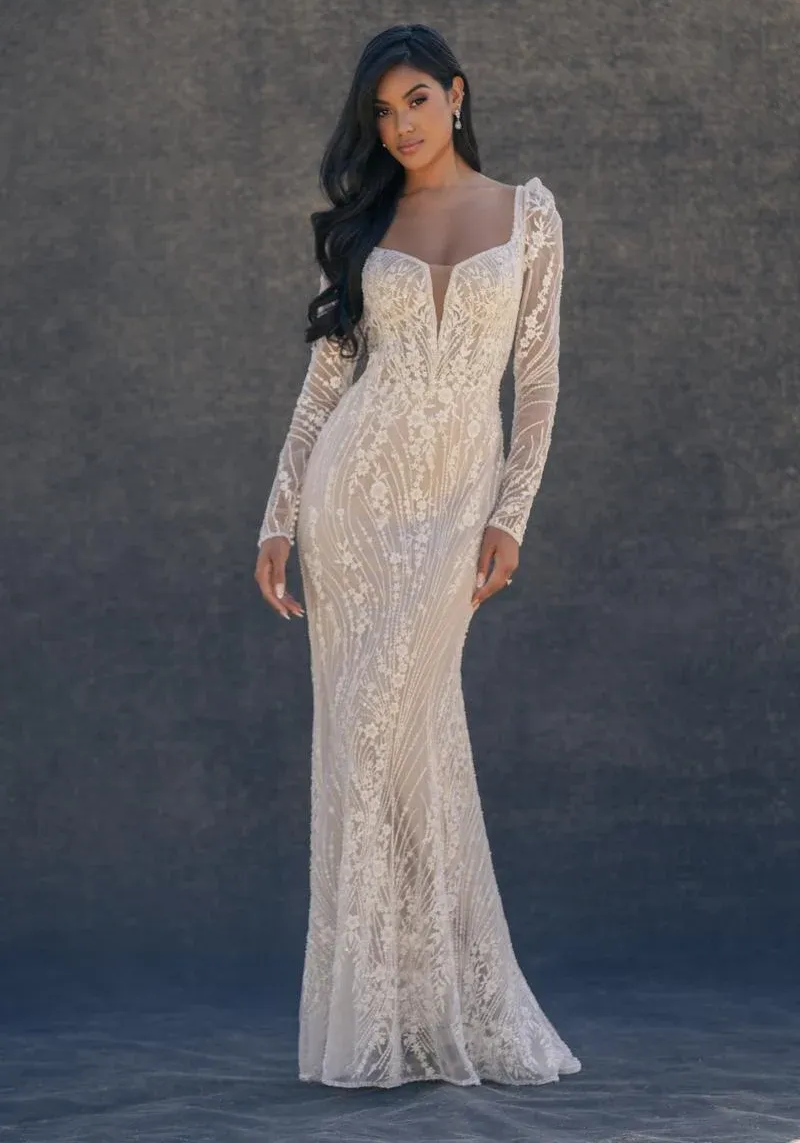 A person wears a minimalist white floor-length wedding gown with thick straps and a fitted silhouette against a grey wall.