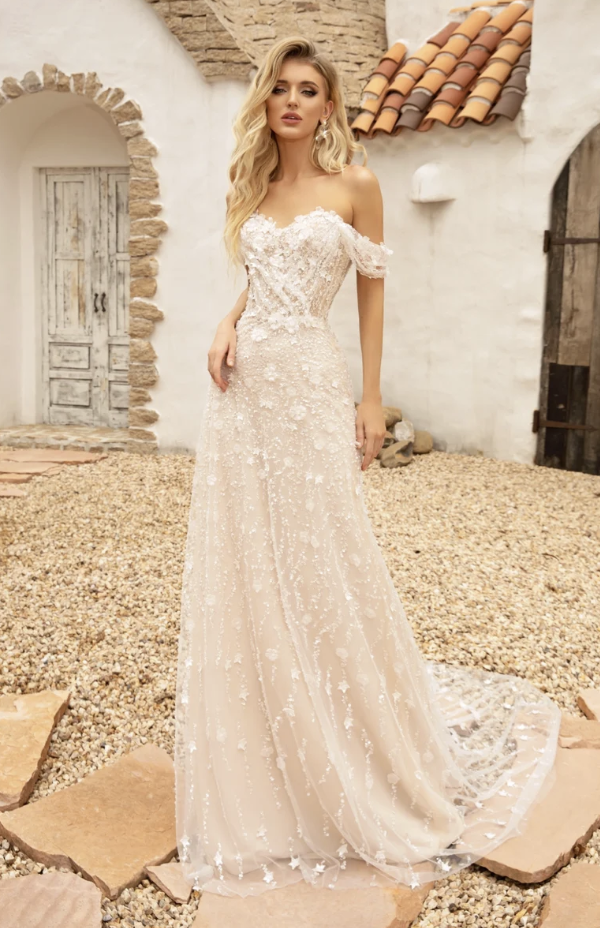 Woman in a white lace wedding dress standing on a beach at sunset.
