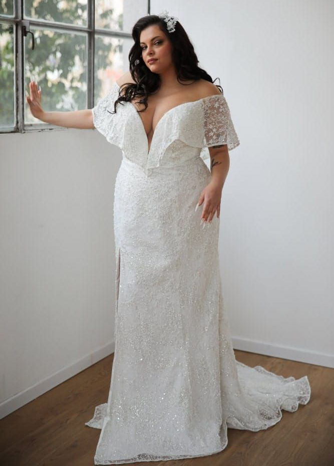 Woman in a white strapless mermaid gown posing indoors by large windows.