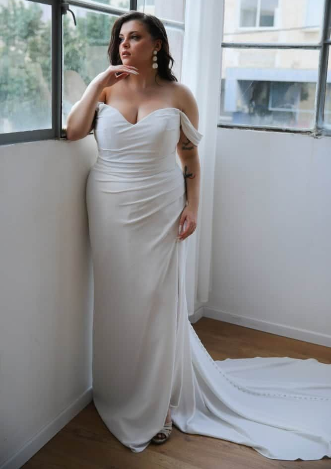 Woman in a white strapless mermaid gown posing indoors by large windows.