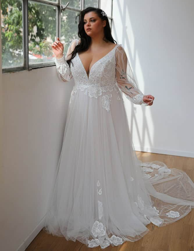 Woman in a white strapless mermaid gown posing indoors by large windows.