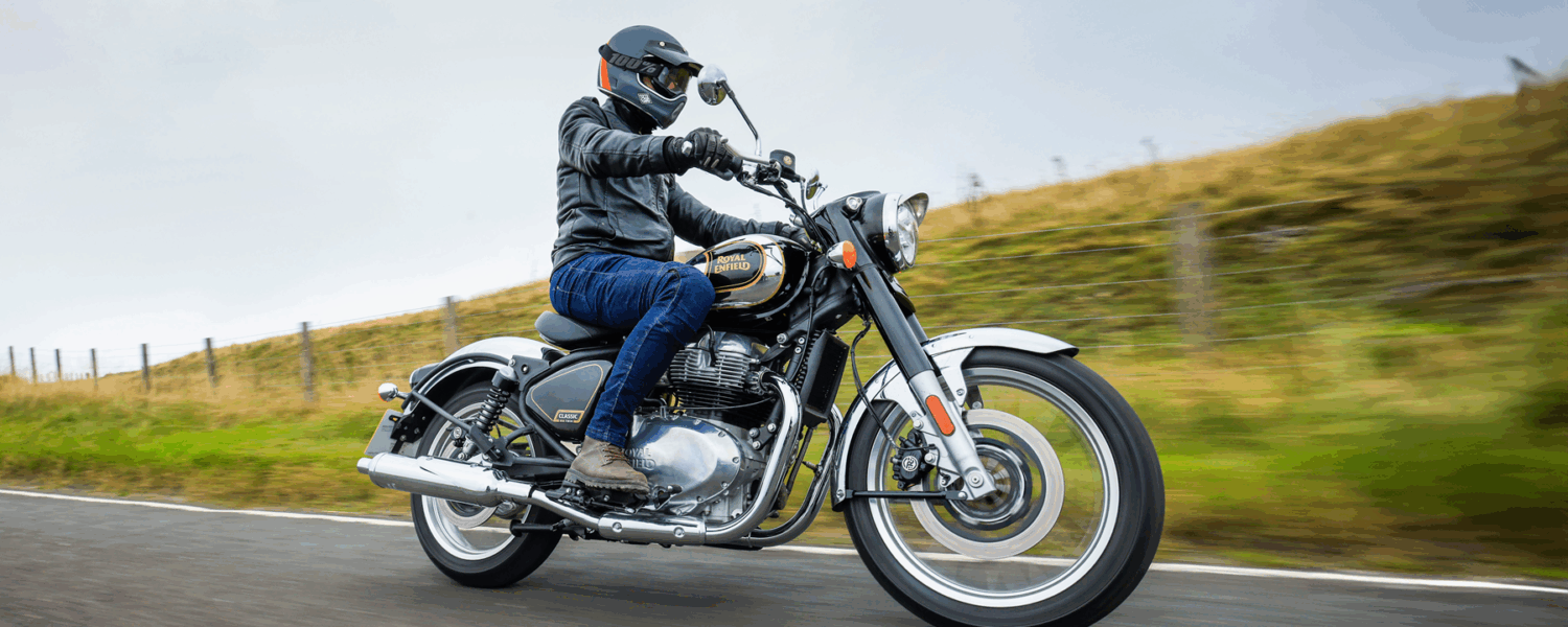 Motorcyclist riding a chrome bike on a road beside a grassy hillside
