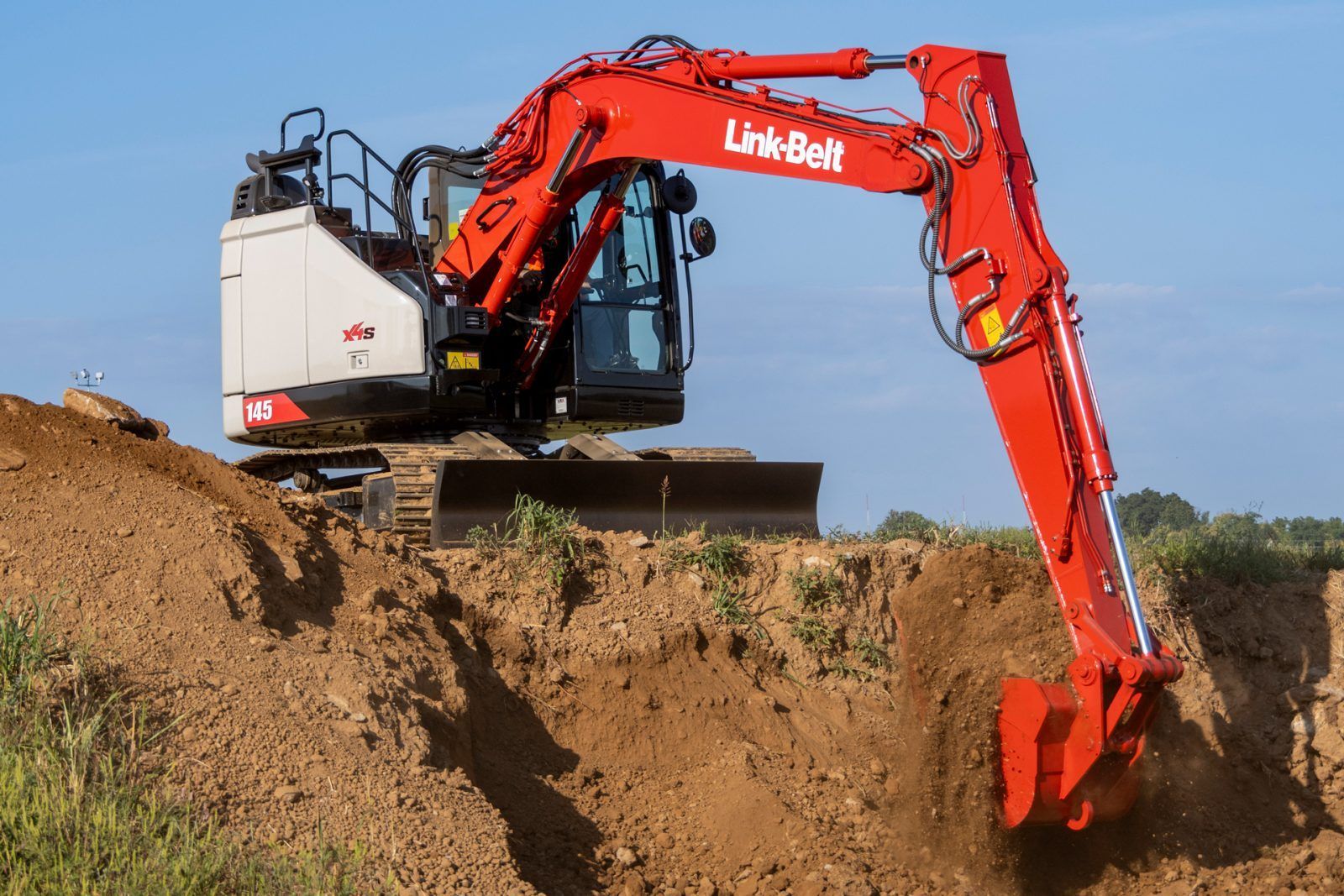 Red excavator digging into a dirt embankment on a construction site under a clear sky