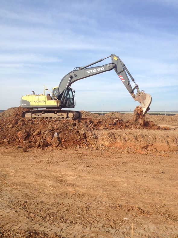 Yellow excavator on a dirt embankment, arm extended over a construction site under a blue sky