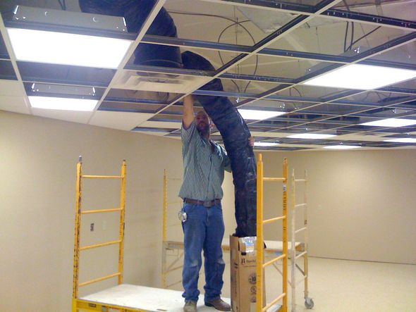 Two workers on ladders installing a ceiling grid in a vacant room