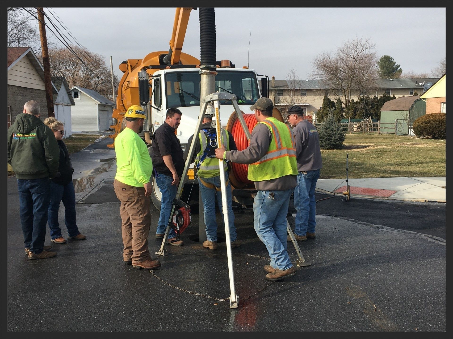 Workers around a survey tripod beside a truck-mounted crane on a residential street