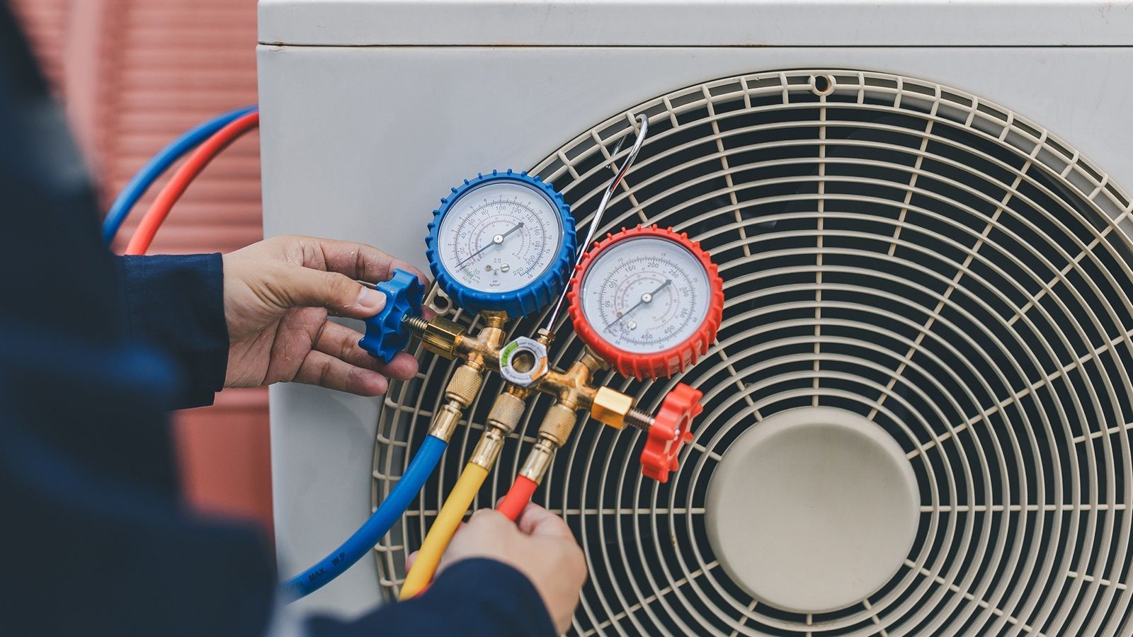 Technician using manifold gauges on an outdoor air conditioner unit for maintenance