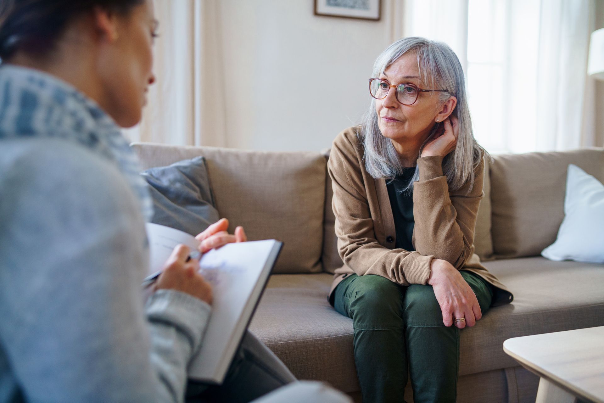 A woman is sitting on a couch talking to another woman.