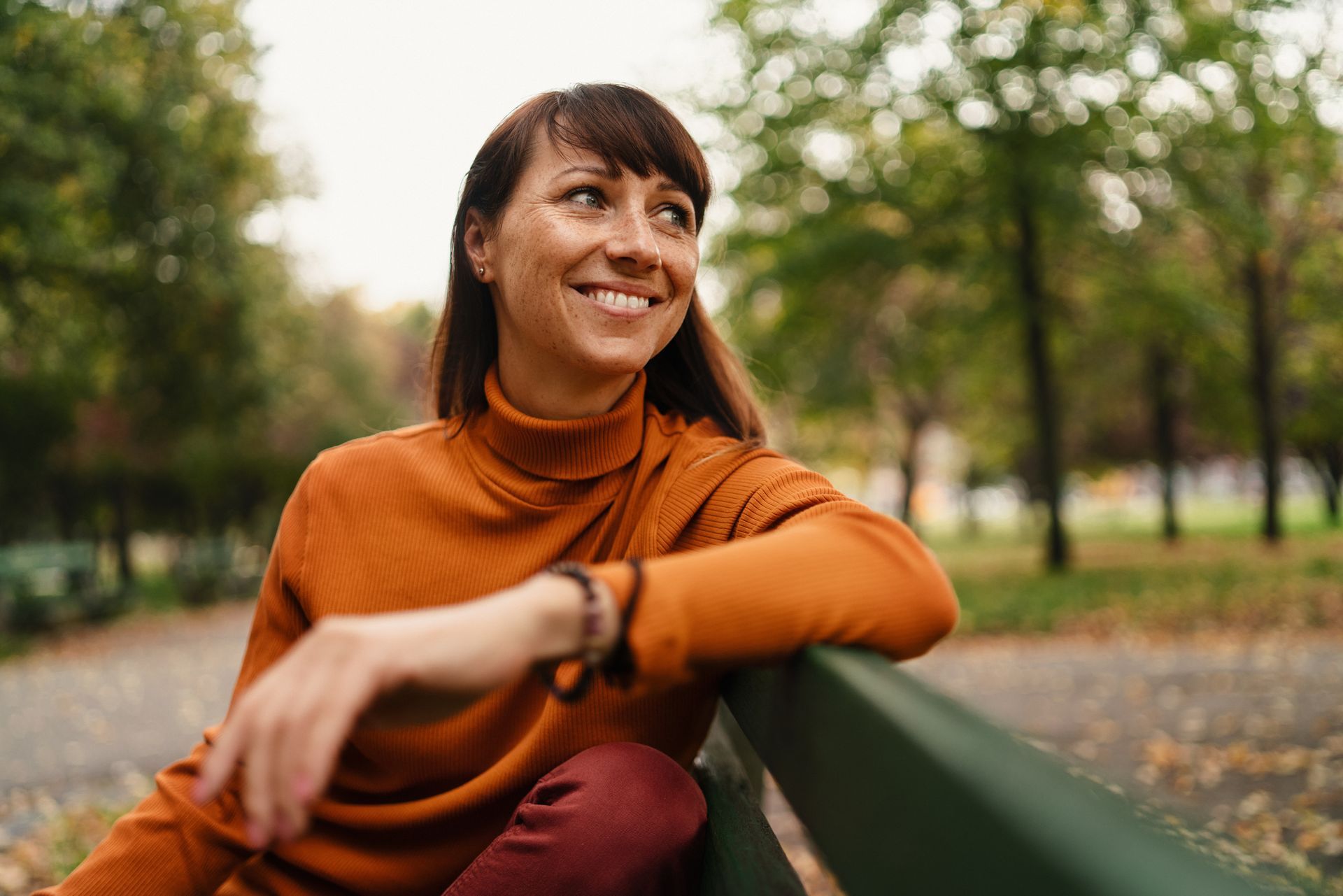 A woman is sitting on a park bench and smiling.