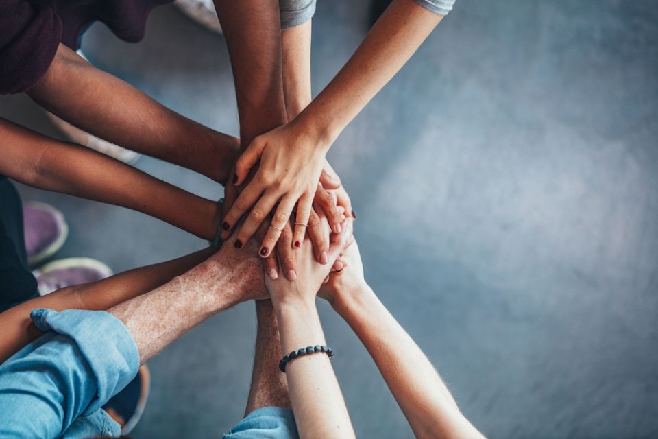 individuals putting hands over each other hands