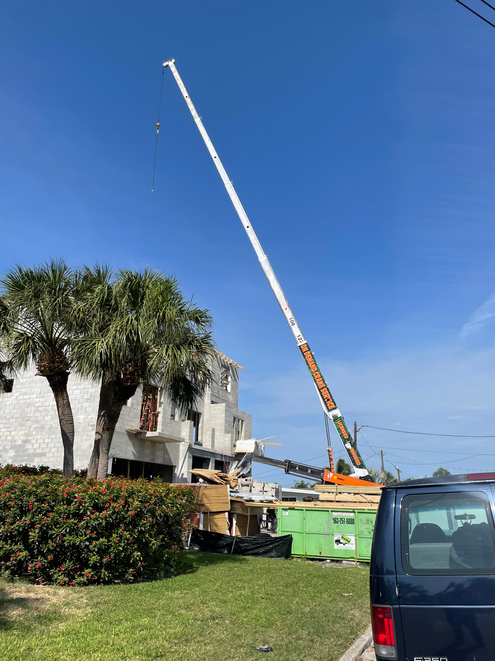 Crane next to building, debris below. Clear blue sky. Orange and white crane boom, green dumpsters.