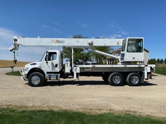 White crane truck on a gravel road under a blue sky, with the crane arm extended.