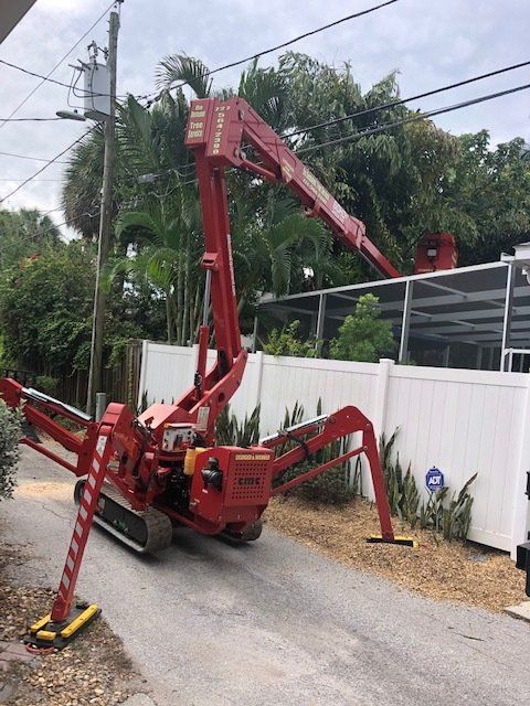 Red spider lift reaching toward a rooftop, parked on a paved driveway near power lines.