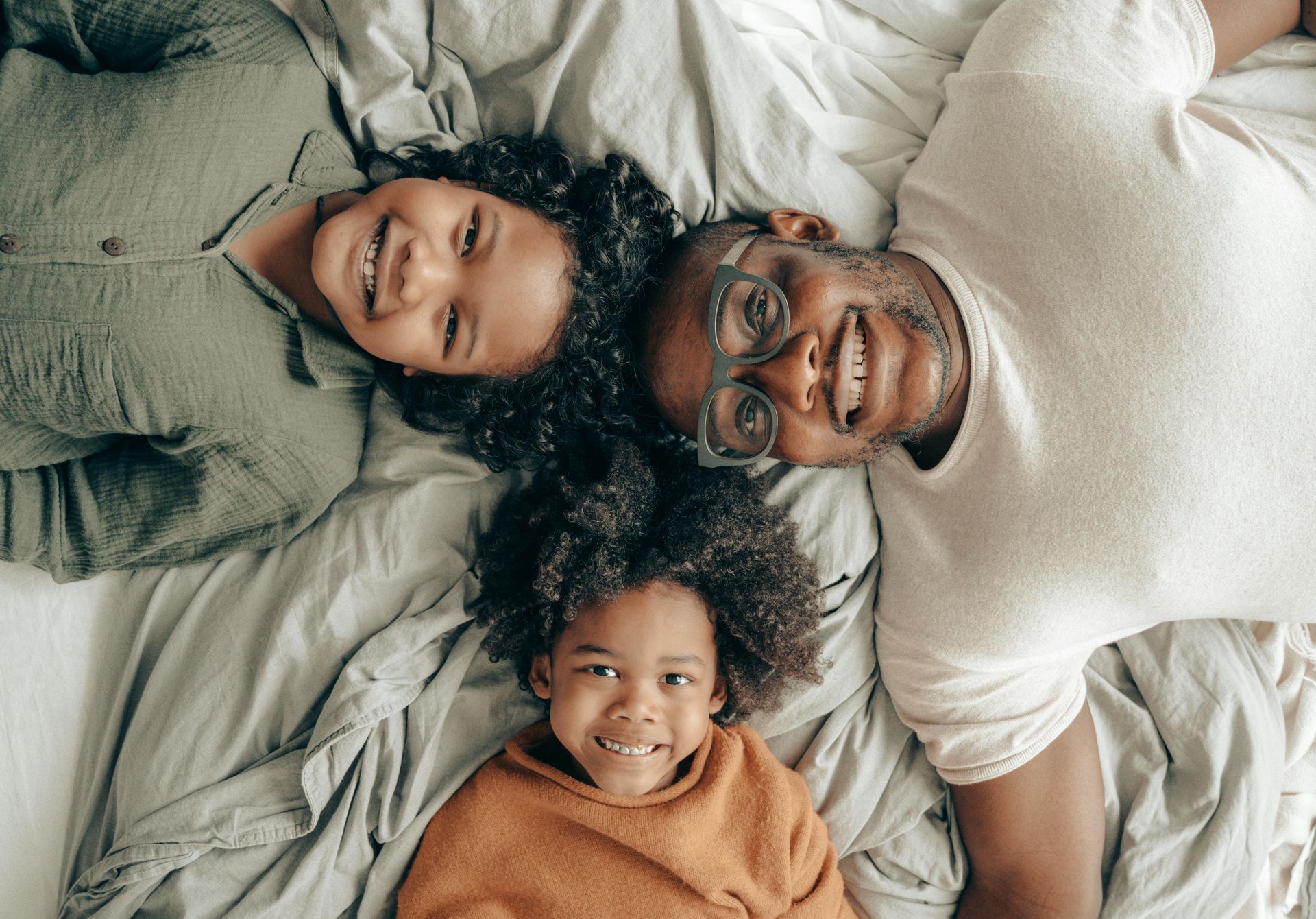 Three people lying on a bed, smiling and looking up at the camera.