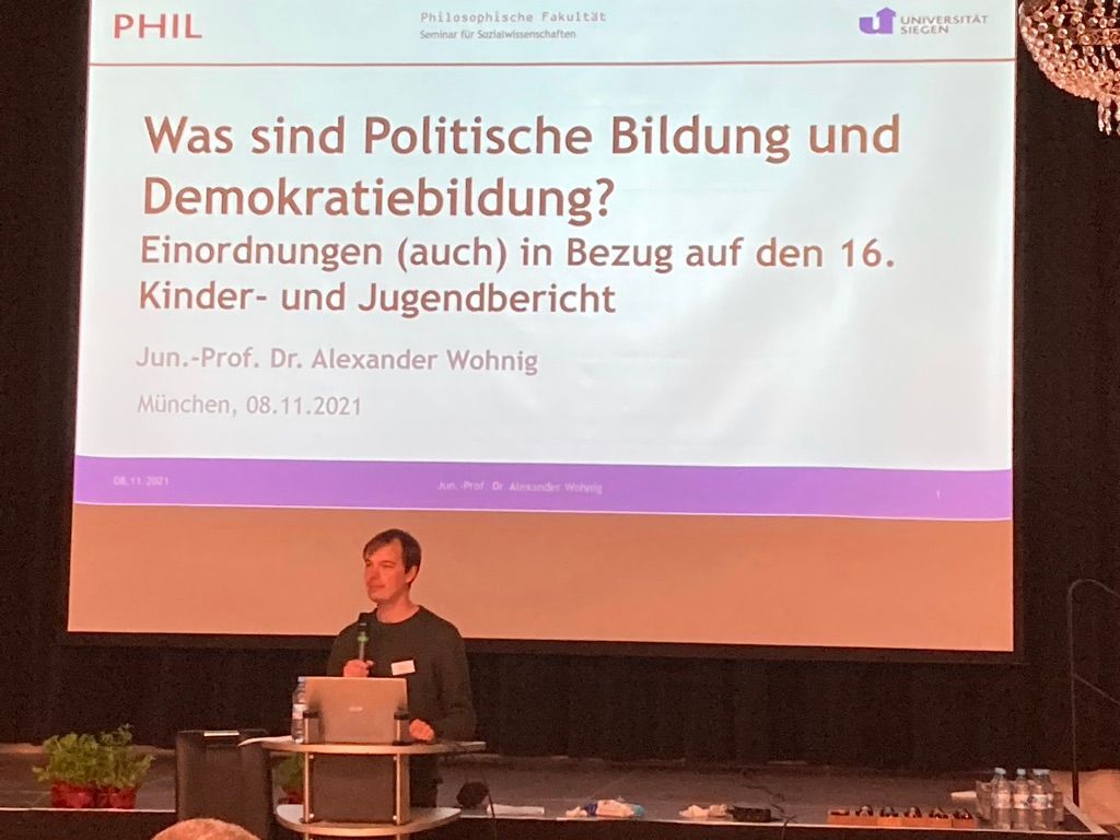 Sprecher am Mikrofon vor der Leinwand 
