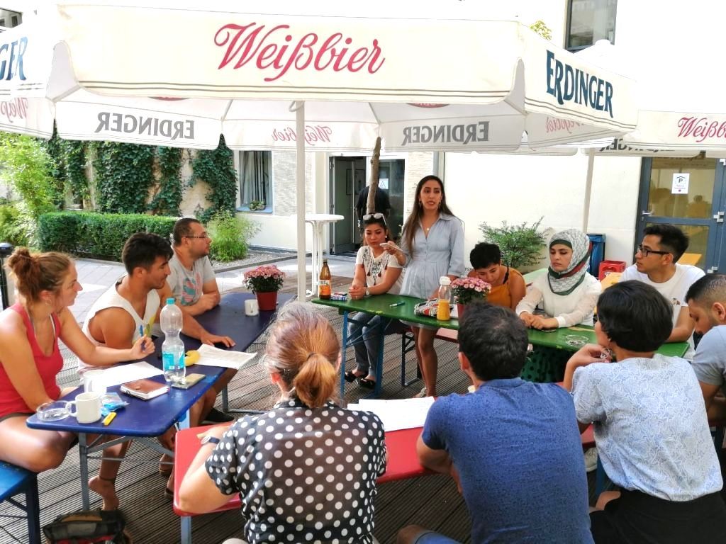 Viele junge Menschen unter Sonneschirmen an Tischen bei Diskussion mit Arbeitsunterlagen