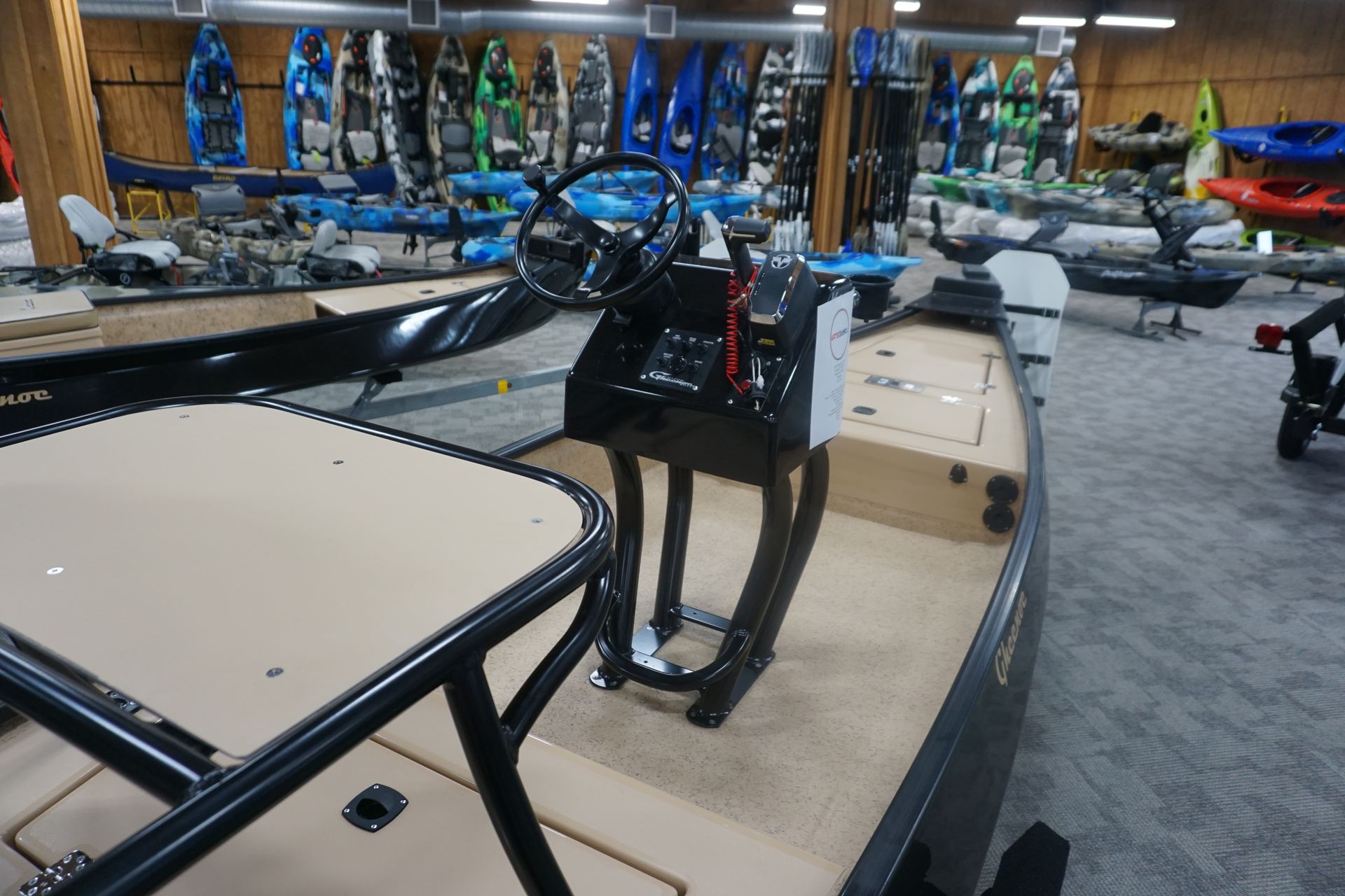 A boat is sitting in a showroom surrounded by kayaks.