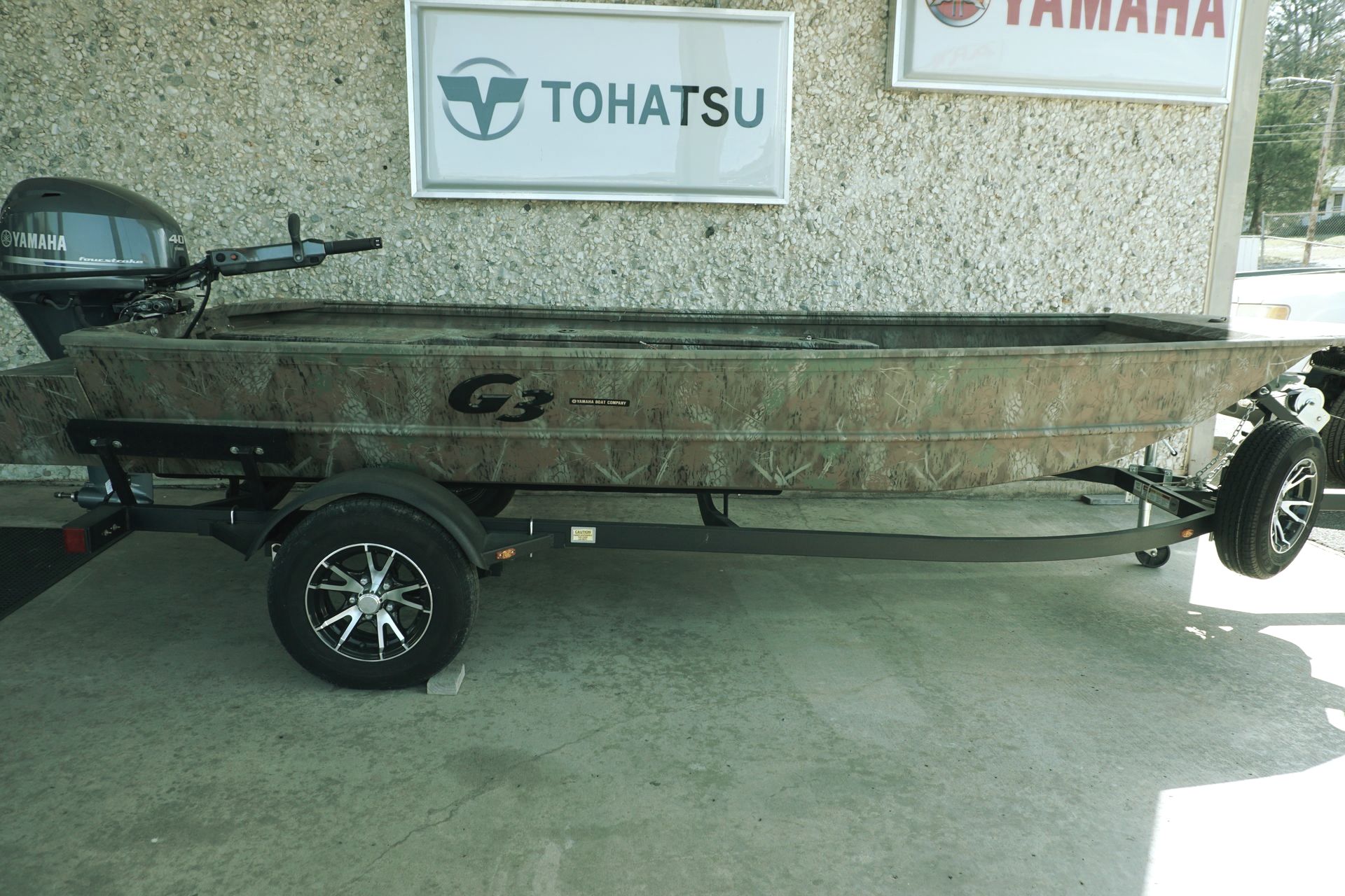 A boat on a trailer is parked in front of a tohatsu sign.