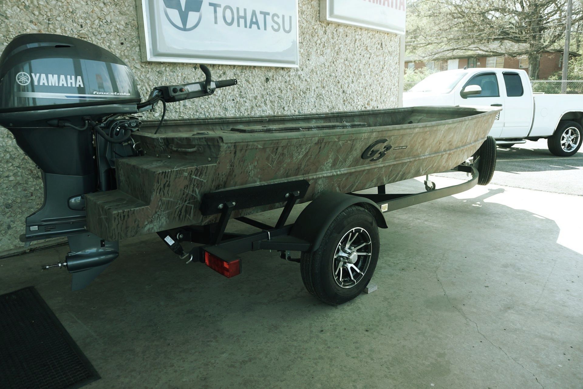 A boat with a yamaha engine on a trailer is parked in front of a tohatsu sign.