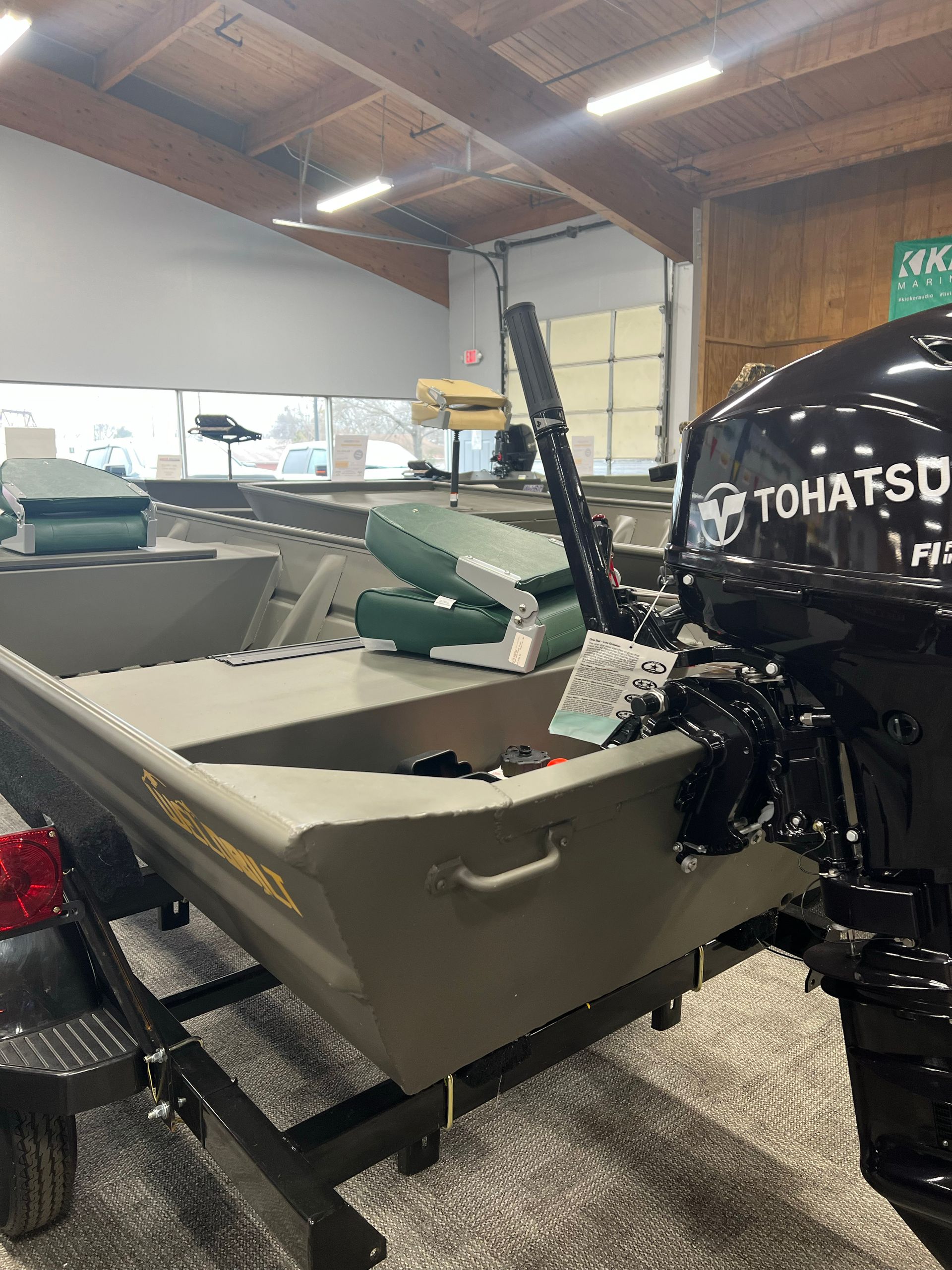 A boat is sitting on a trailer in a garage next to a tohatsu engine.