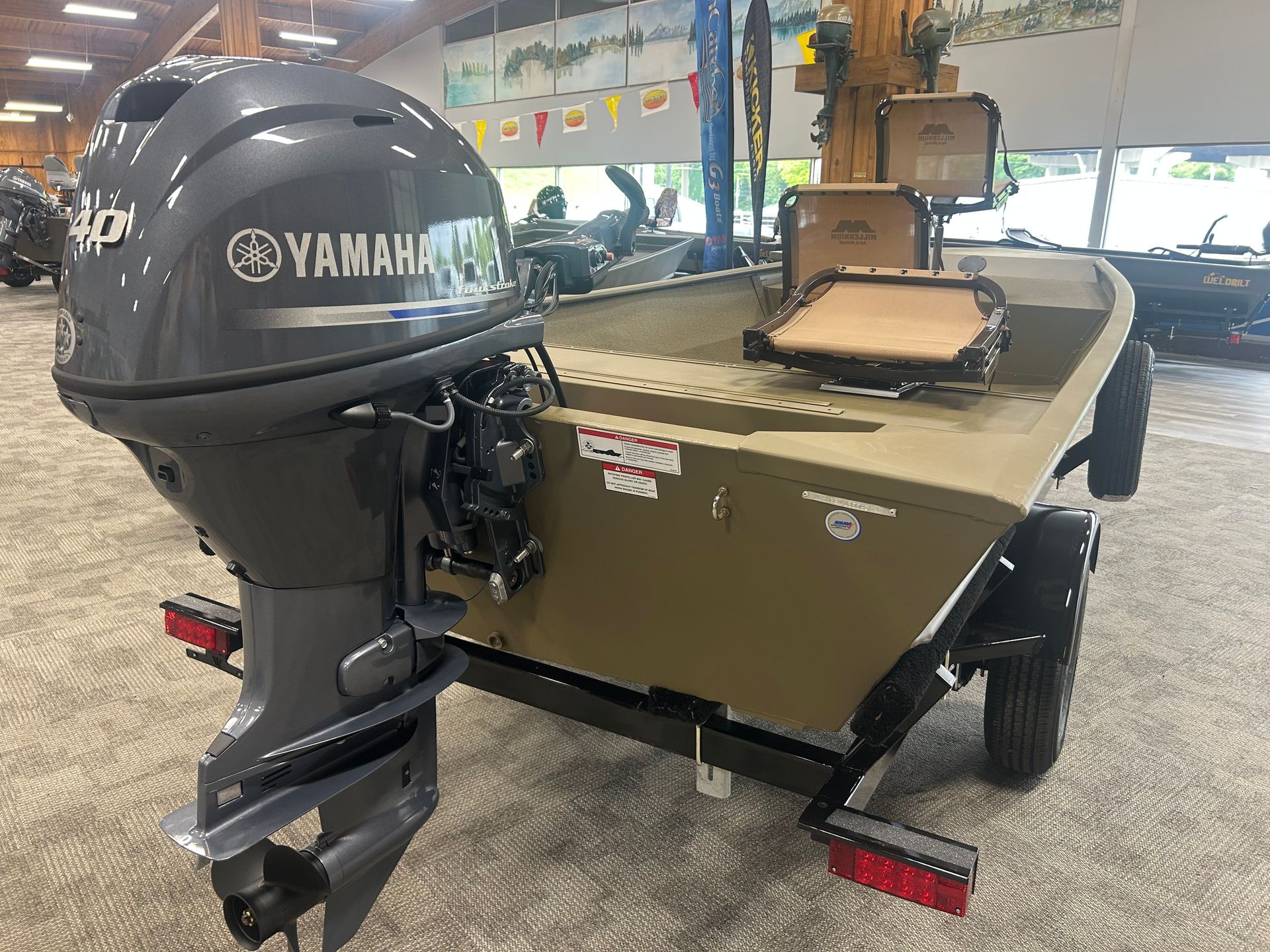 Tan/brown fishing boat with a Yamaha outboard motor on a trailer in a workshop garage.