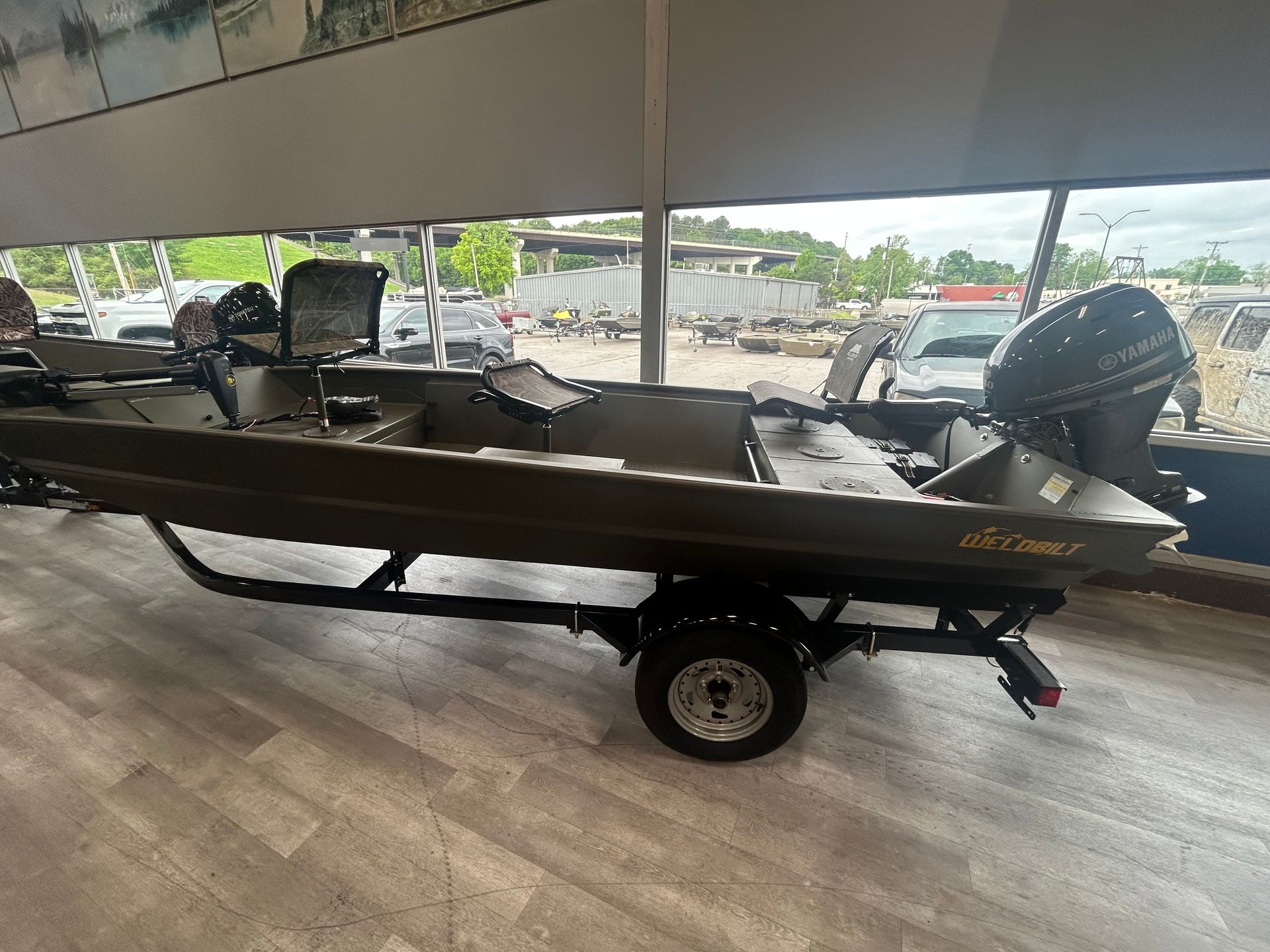 Black fishing boat on a trailer indoors, with an outboard motor and gear under a canopy.