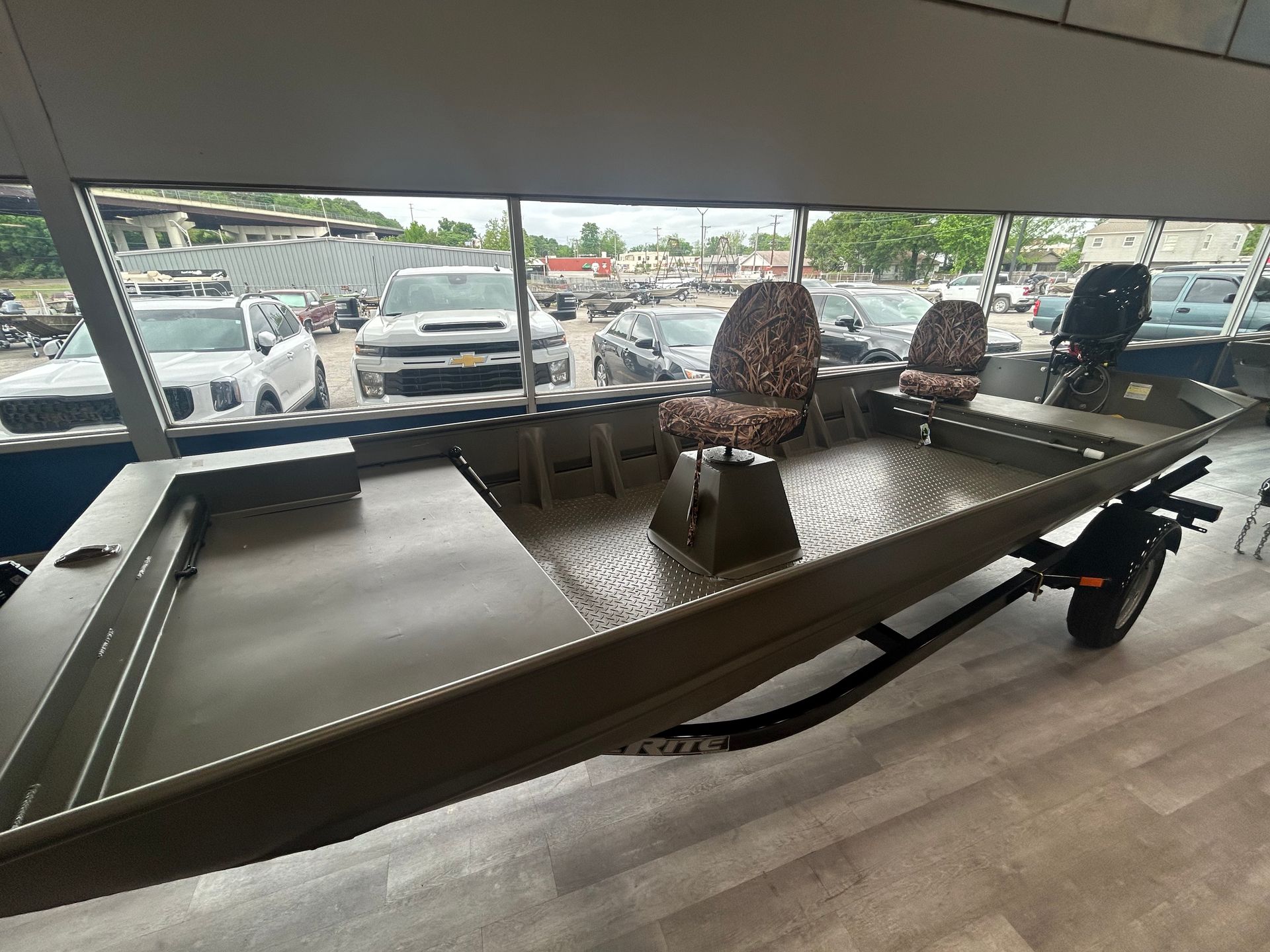 Long fishing boat on display indoors, viewed from the front with open seating and dark hull.