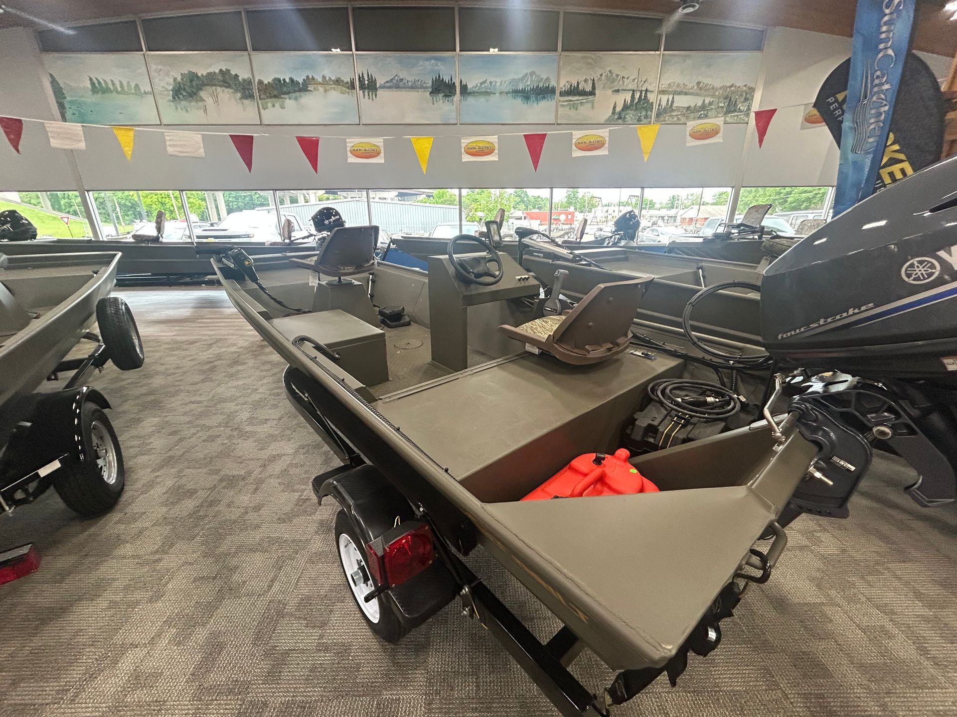 Angler boat displayed indoors at a showroom, with a tan deck and black motor under colorful pennant flags.