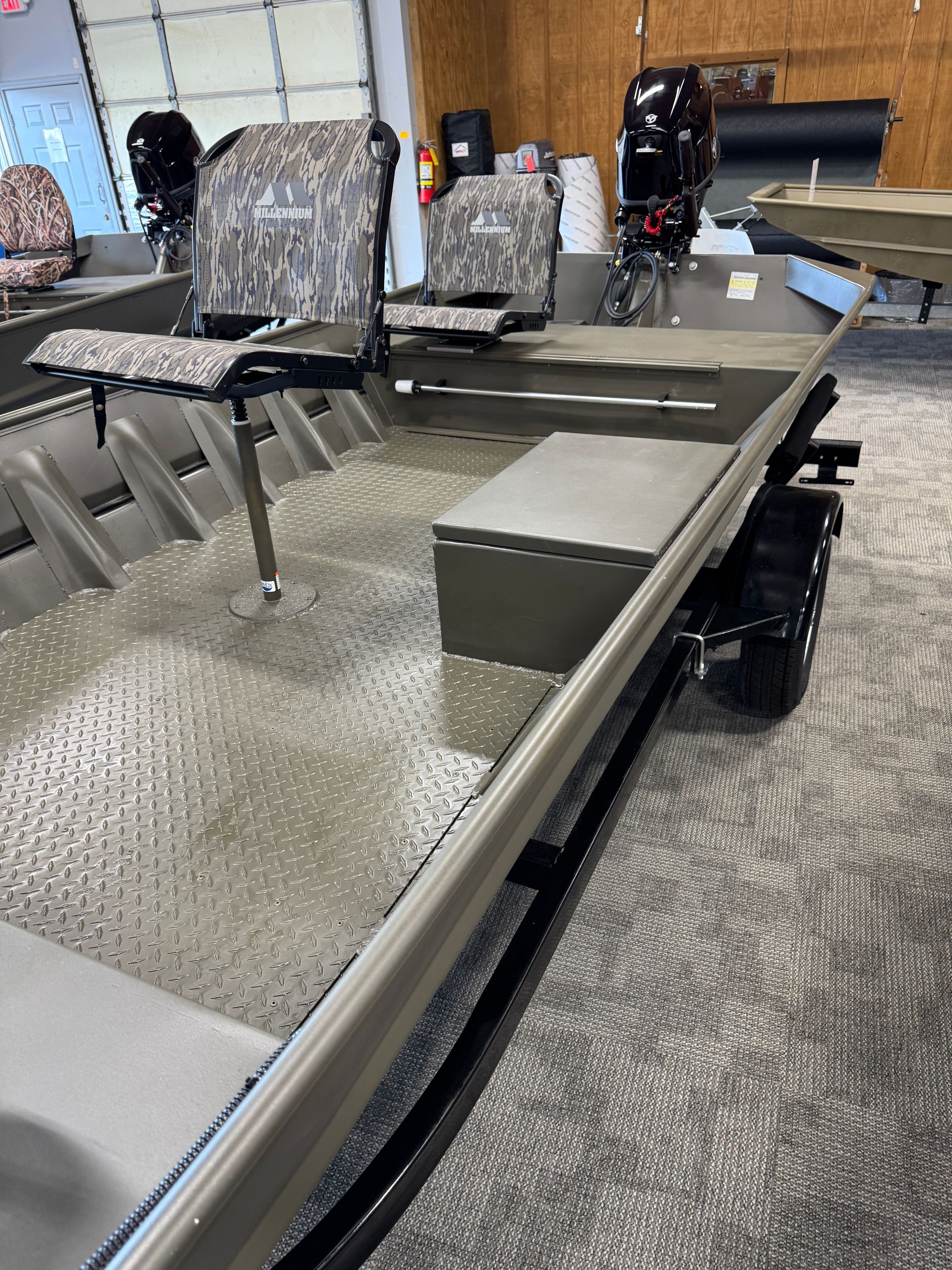 Camouflaged aluminum boat interior with padded seats, steering console, and metal flooring in a showroom