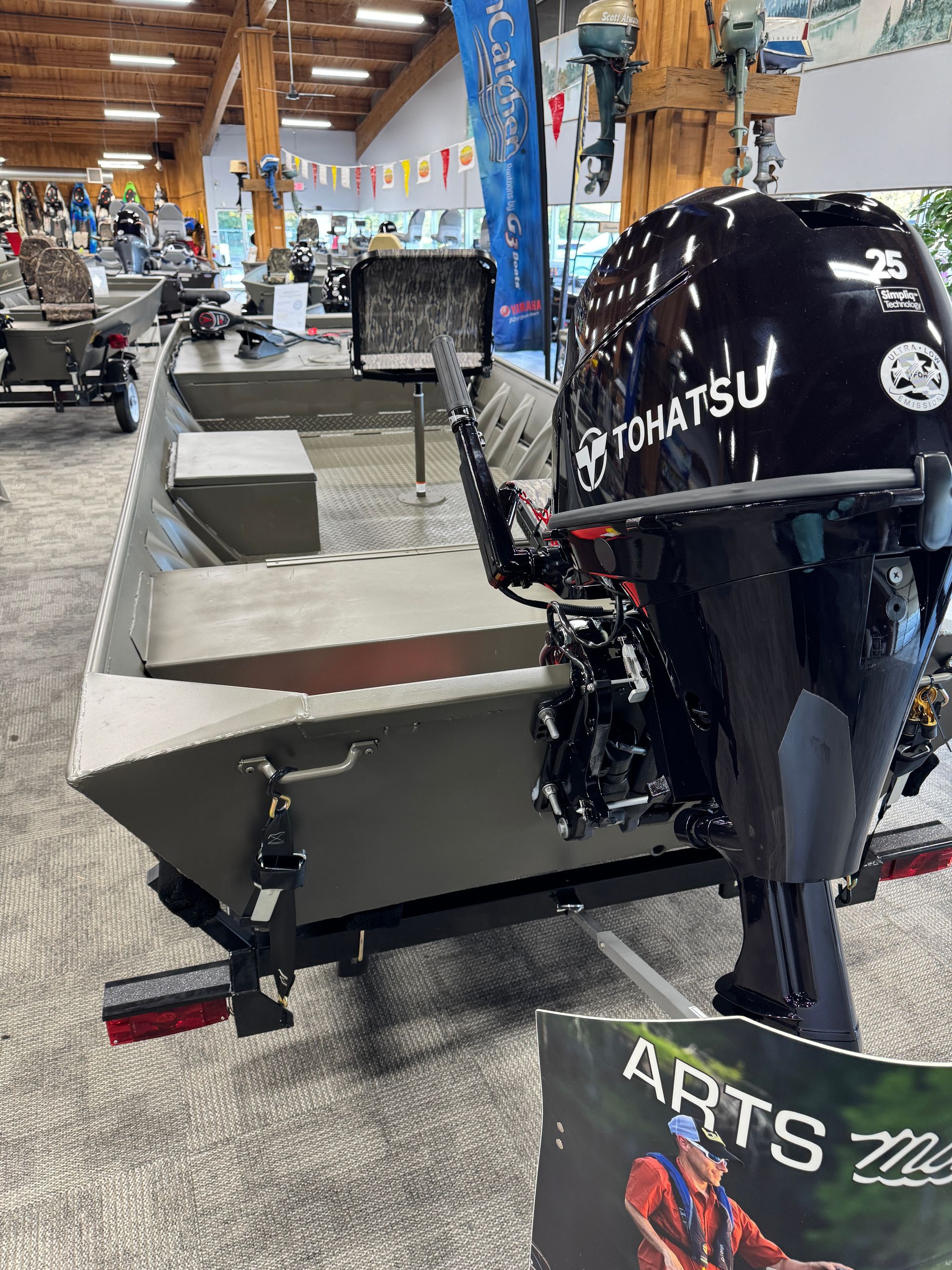 Small aluminum fishing boat with a black Komatsu outboard motor in a workshop showroom.