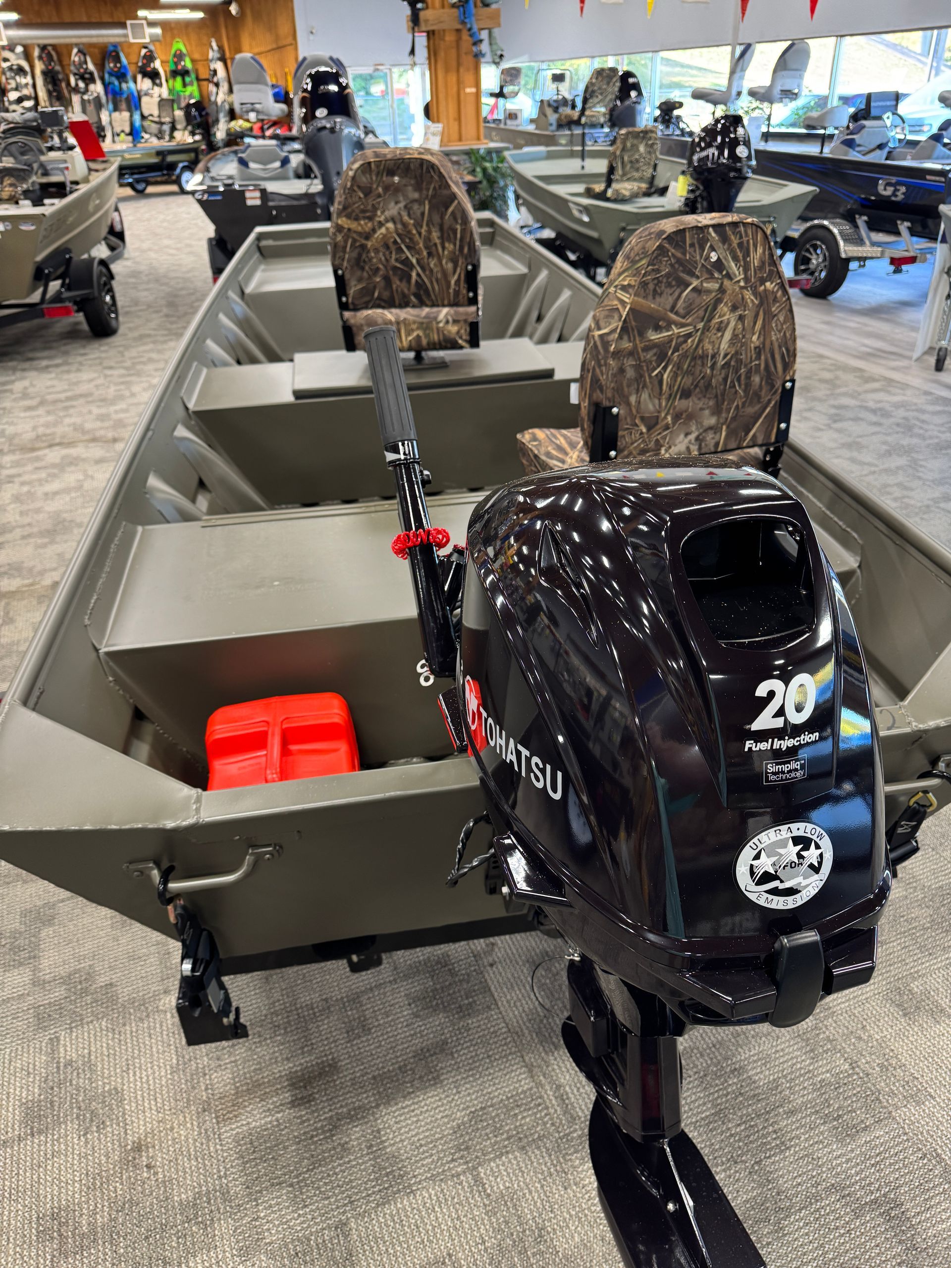 Camouflaged aluminum fishing boat on display at an indoor showroom, with a black outboard motor