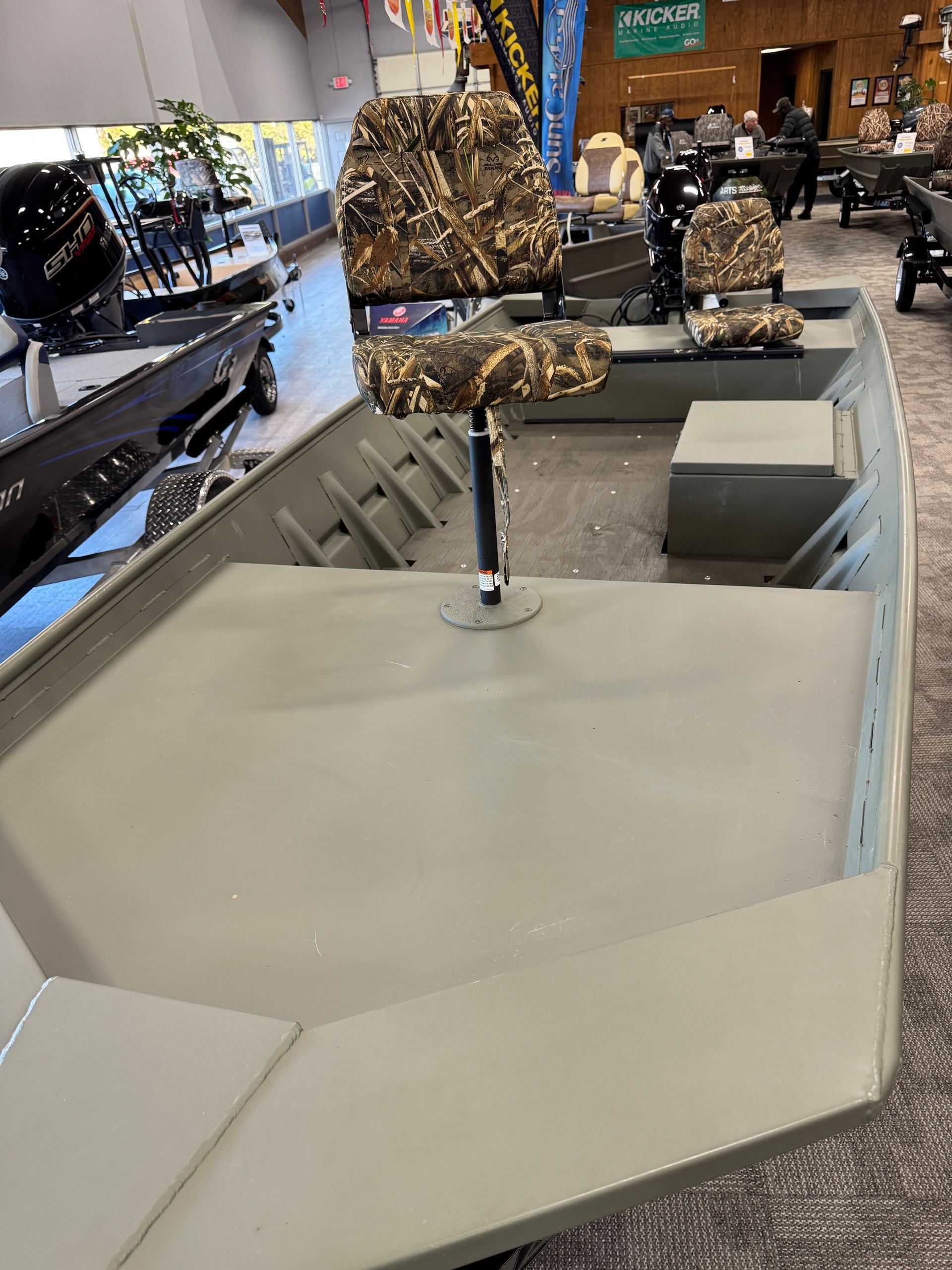 Small camo-pattern hunting boat interior displayed in a showroom, with gray deck and seats